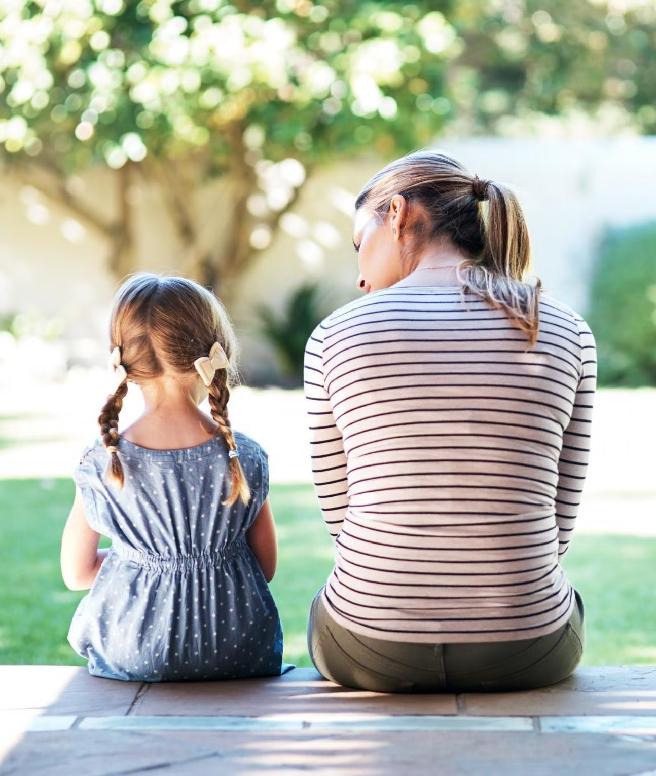 Mother and child sat with backs towards the camera. Mother talking to daughter.